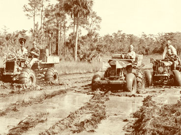 Early Swamp Buggy race in 1949.  Pictured L to R:  Leon McCormick driving Rambler with A.P. Ayers in turkey hat.  Ed Frank, inventor of the swamp buggy, riding in Tumble Bug.  Palmer Harris behind the wheel of Whiskey with Carl Scott riding along.