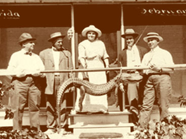 Group of 5 people posing on steps of Bamboo Cottage (Hachmeister's home) with alligator slung on pole.  Pictured L to R:  2 men & 1 woman unidentified, George Hendrie, John Hachmeister.  February 12, 1914. (John Hachmeister Collection)